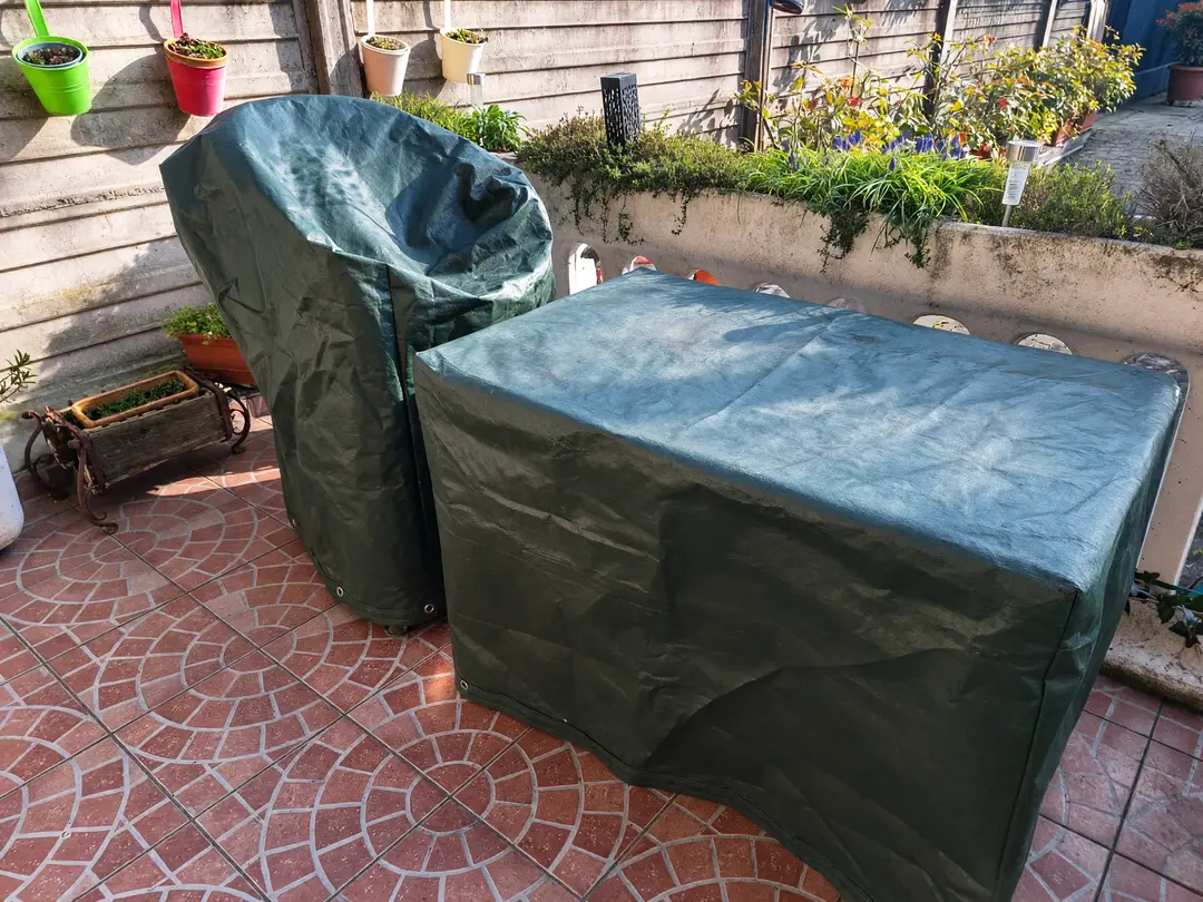 Garden table and chair under made-to-measure green covers with eyelets, on a tiled patio