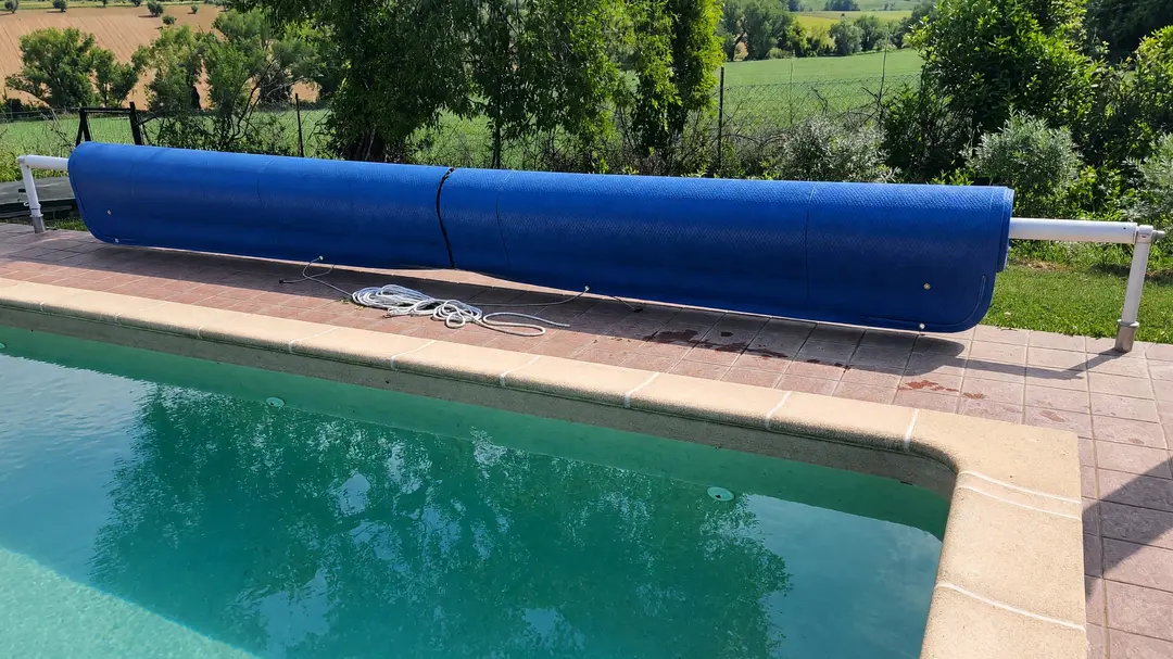 Blue foam cover rolled up on a roller on uprights, beside an in-ground pool