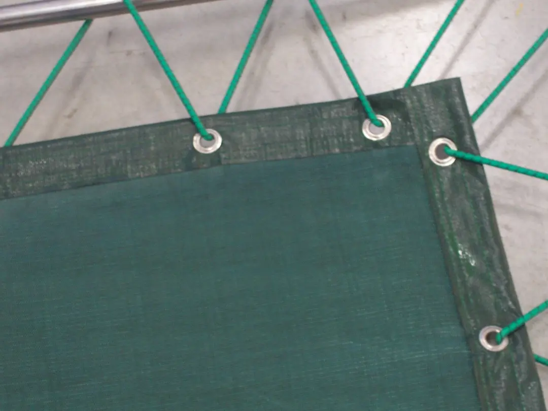 Close-up of the corner of a green Eltex mesh shade cloth, with metal eyelets and elastic cords